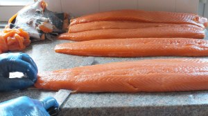 Salmon skinning with completed salmon in the background